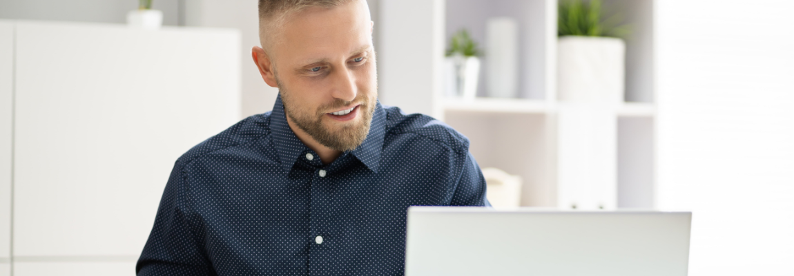 Man in a navy shirt smiling at a laptop screen in a bright office