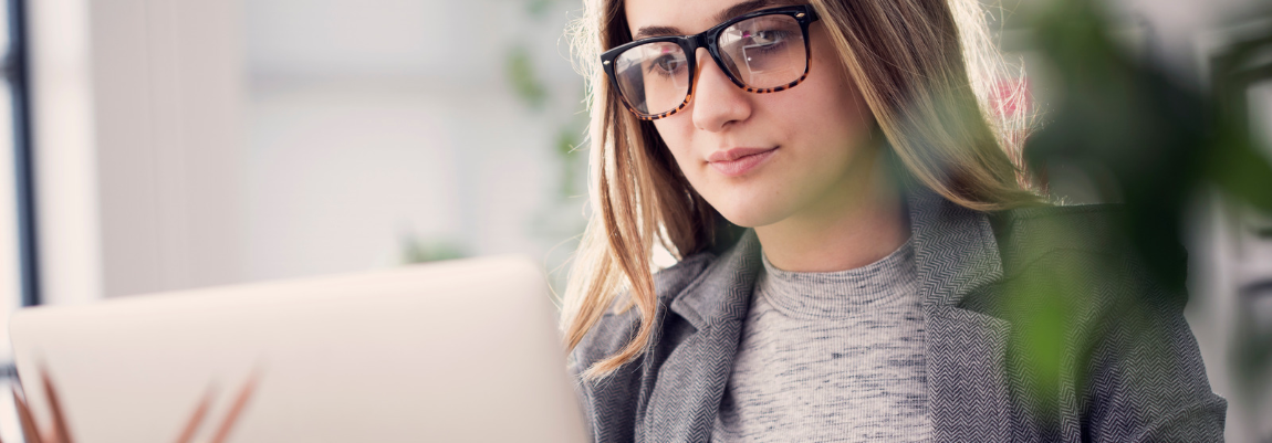 Woman wearing glasses working on a laptop in a bright office